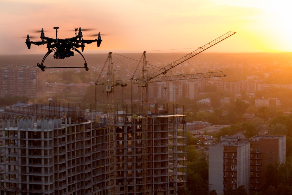 Drone surveying construction of large building with cranes at sunset