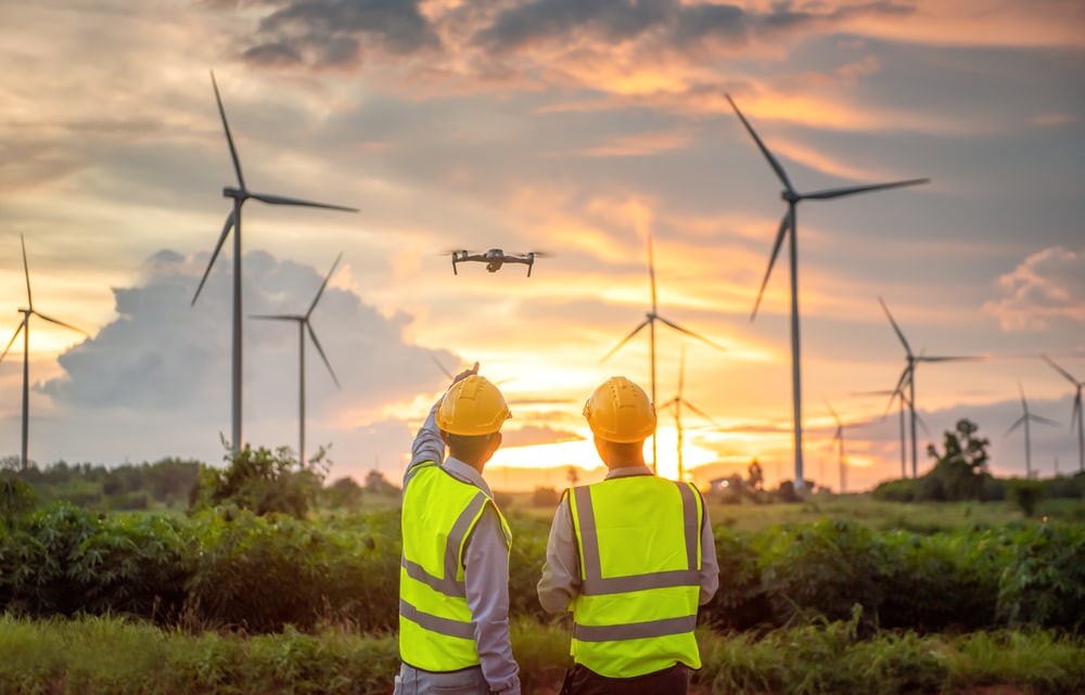 Engineers testing drone surveying wind farm at sunset